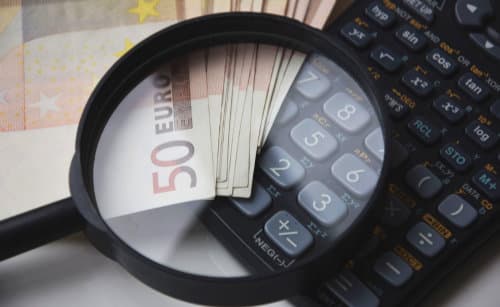 Handlupe über Geldbündel aus 50 Euro Geldscheinen und Taschenrechner